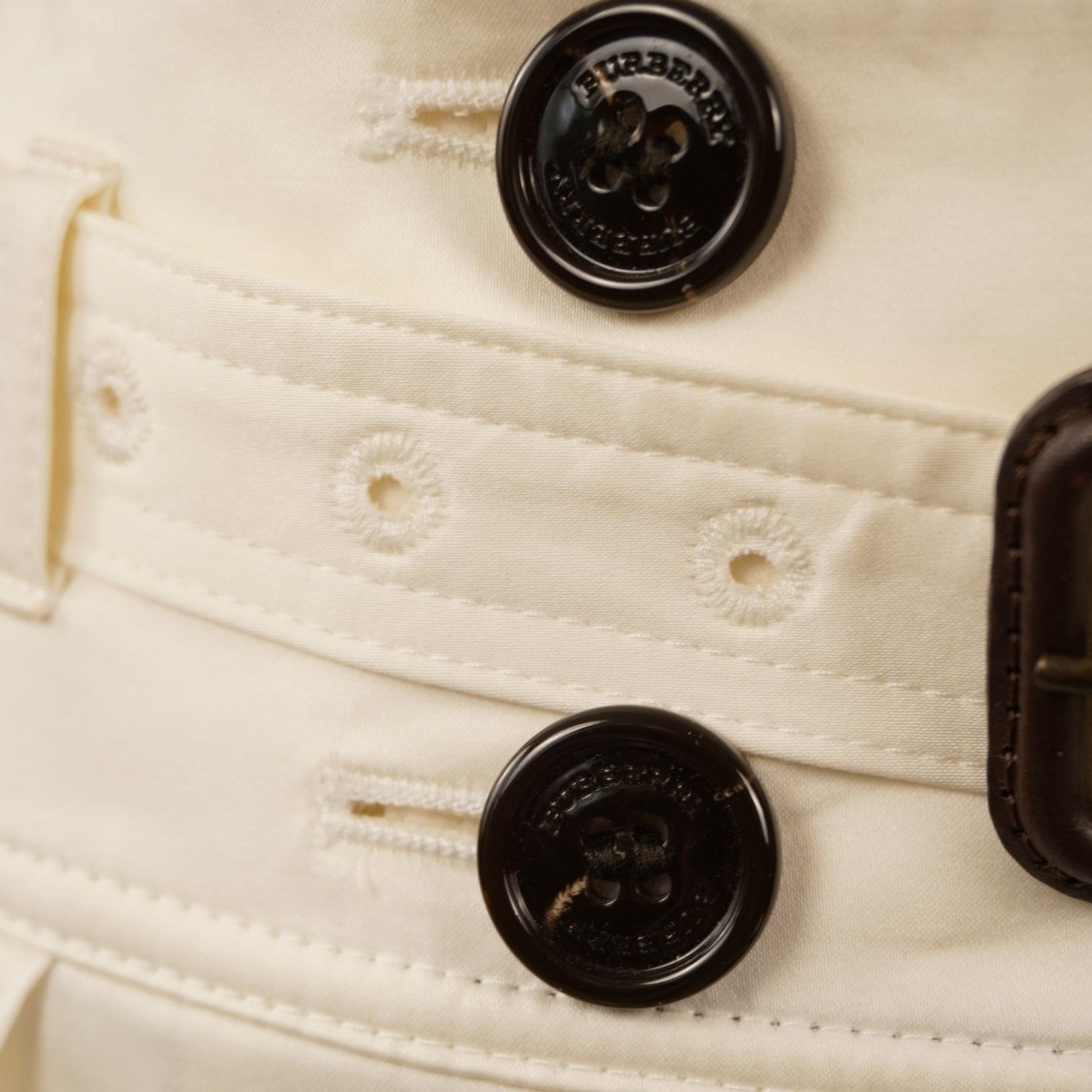 Dettaglio ravvicinato dei bottoni scuri tartarugati con marchio Burberry inciso sulla parte frontale della gonna bianca.