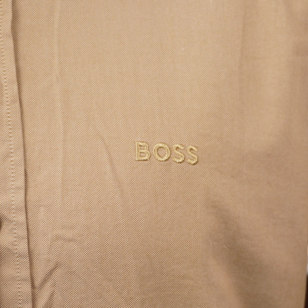 Inquadratura macro del tessuto in cotone organico beige che evidenzia il logo BOSS ricamato tono su tono sul petto.
