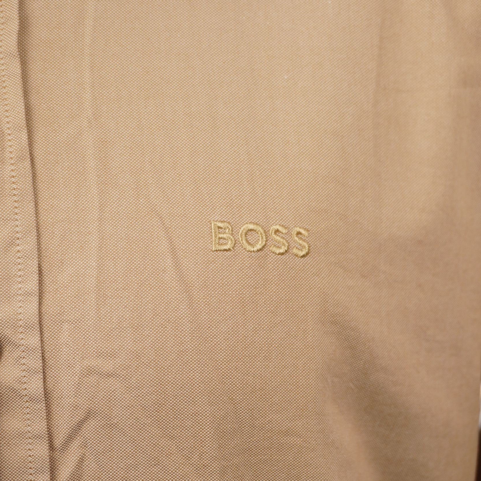 Inquadratura macro del tessuto in cotone organico beige che evidenzia il logo BOSS ricamato tono su tono sul petto.