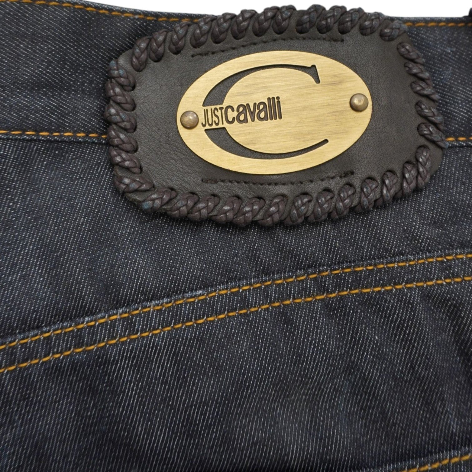 Macro del patch in cuoio scuro con l'esclusivo stemma metallico dorato a rilievo e il monogramma del brand Just Cavalli.