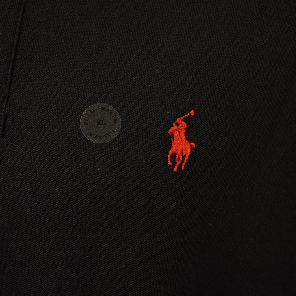 Dettaglio ravvicinato della trama del cotone piqué nero e del ricamo rosso del brand.