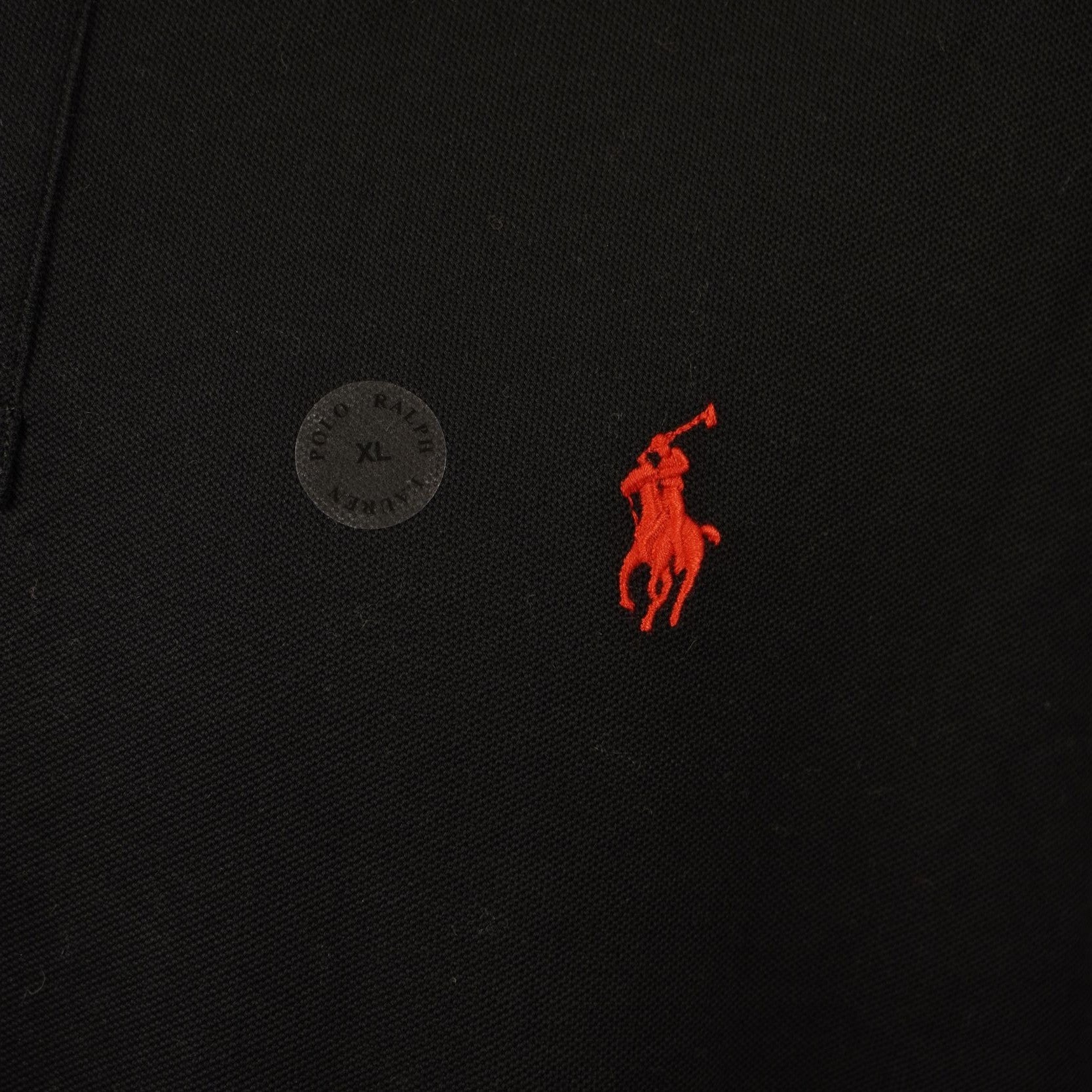 Dettaglio ravvicinato della trama del cotone piqué nero e del ricamo rosso del brand.