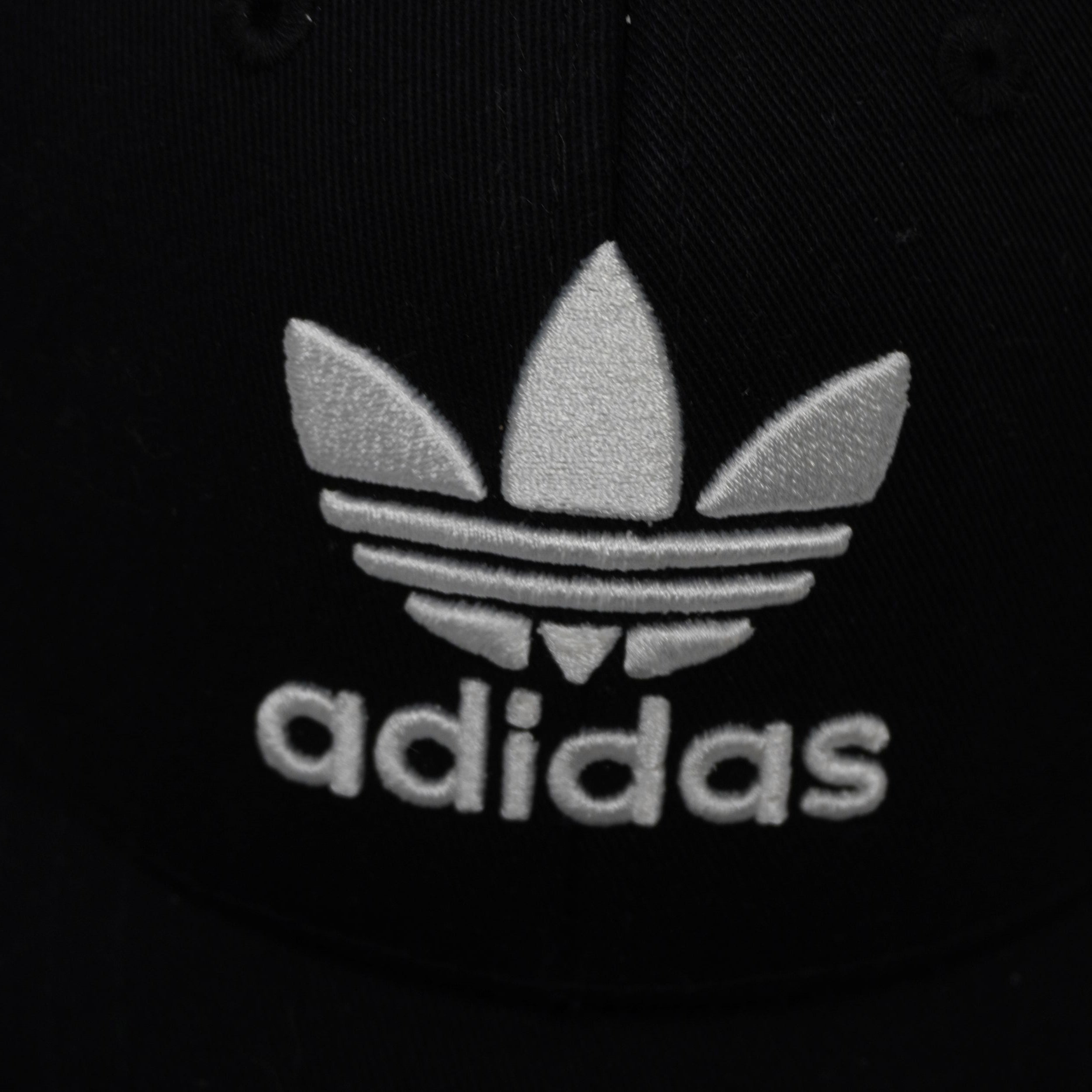 Primo piano ravvicinato in alta definizione del logo del trifoglio Trefoil Adidas ricamato in rilievo bianco su cotone nero.