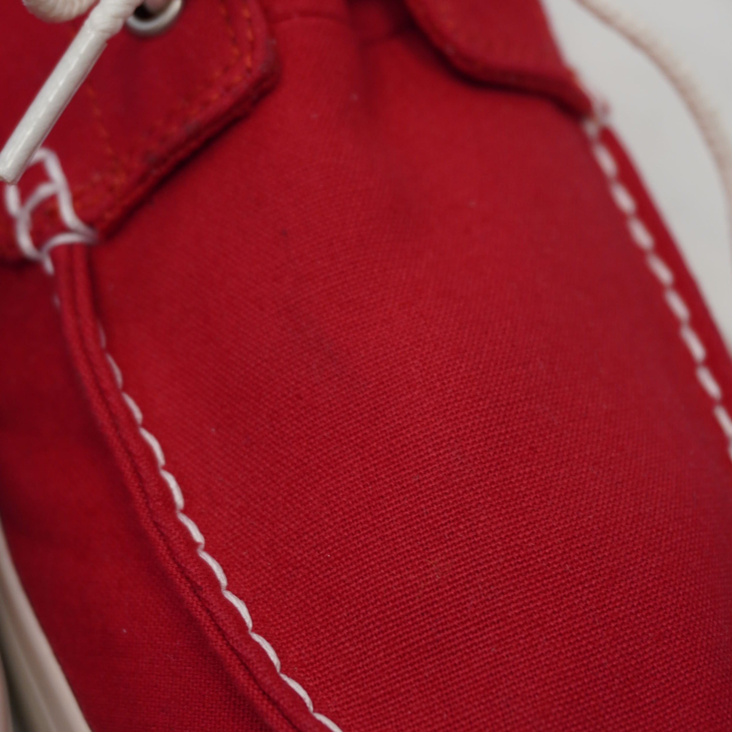 Zoom macro sulla struttura del tessuto in canvas rosso e sulle cuciture bianche della vaschetta frontale.