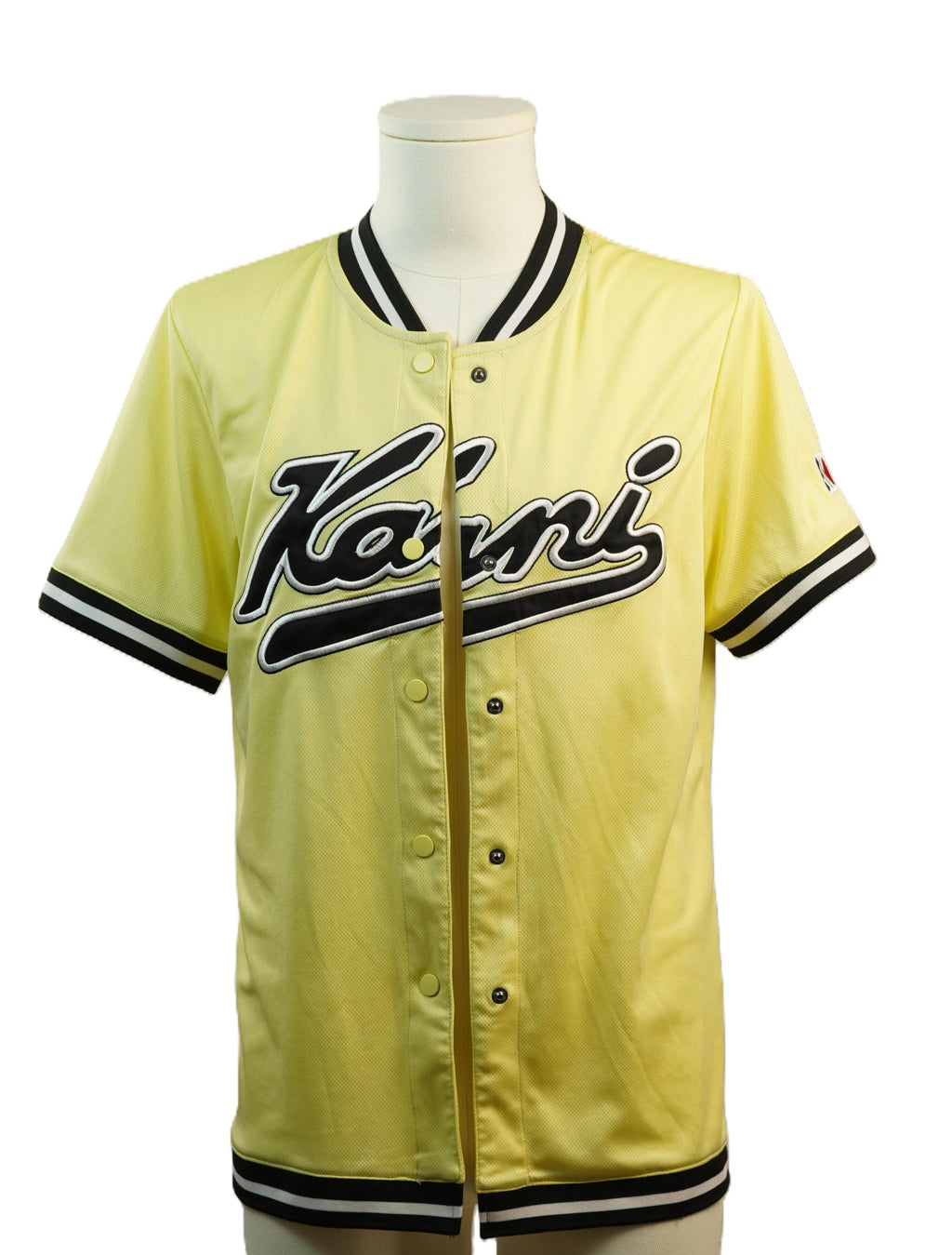 Vista frontale di una maglia da baseball vintage Karl Kani gialla su un manichino, con bottoni sul davanti, profili neri e bianchi a contrasto e ricamo sul petto.