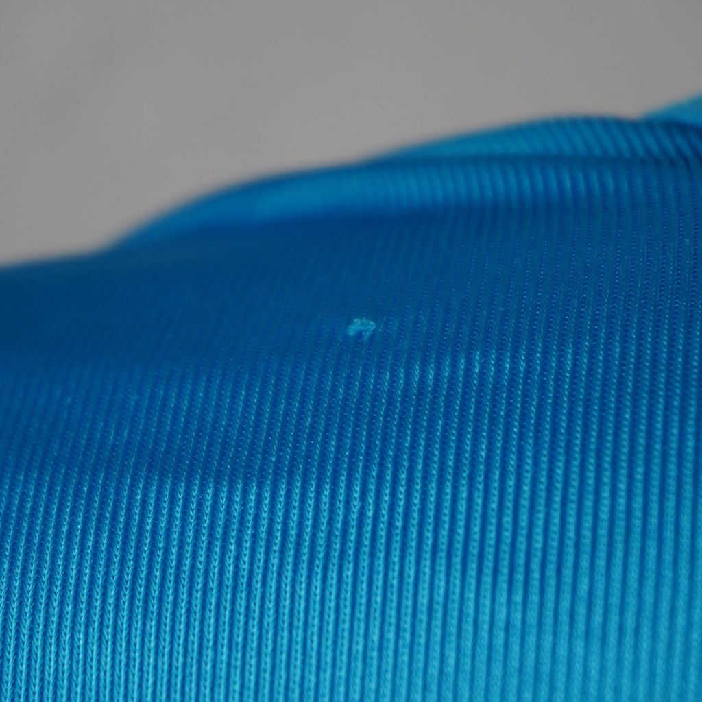 Evidenza del piccolo filo tirato sulla trama del tessuto azzurro segnalato nella descrizione del capo.
