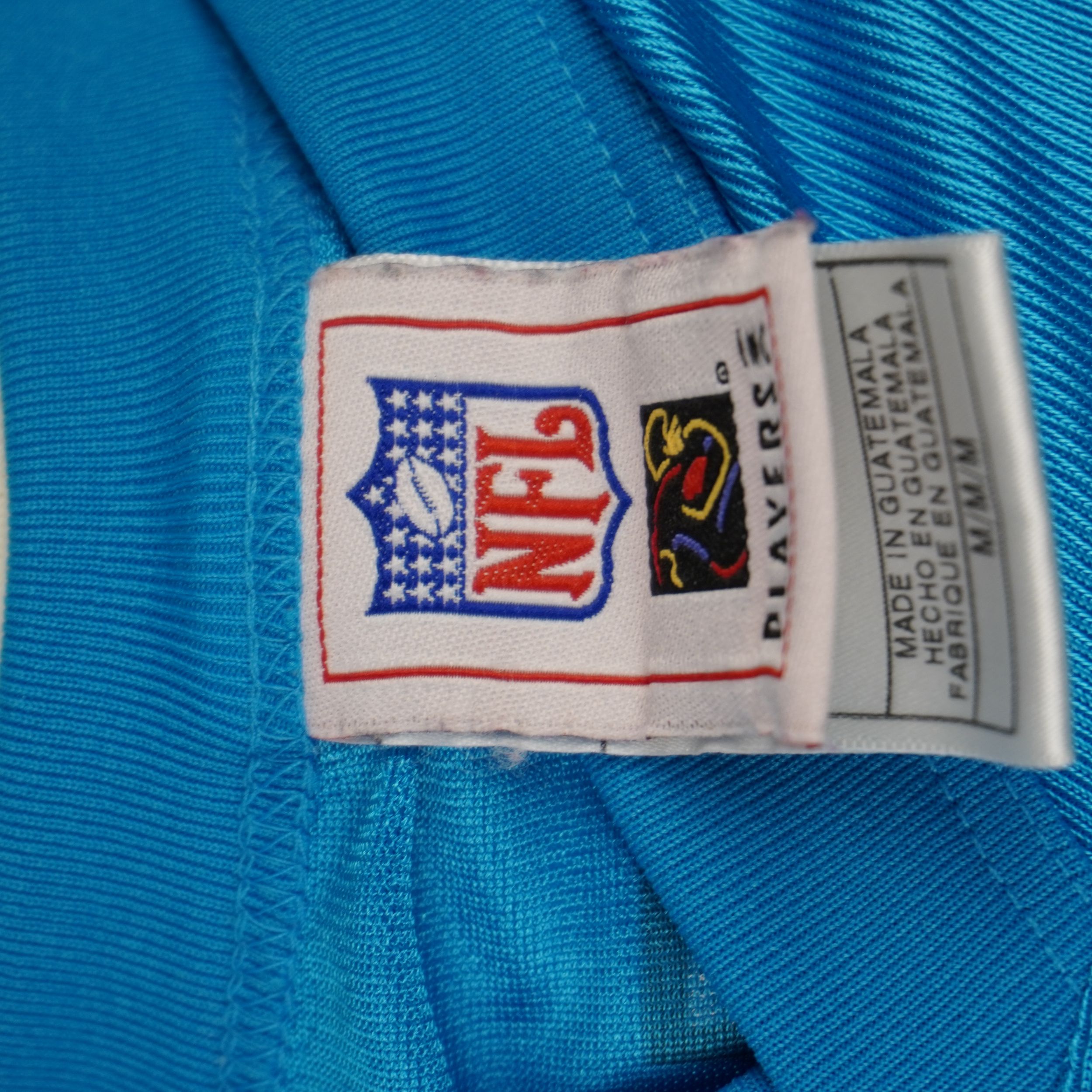 Tag di autenticità NFL Players e brand Reebok applicato sul bordo inferiore esterno della maglia.