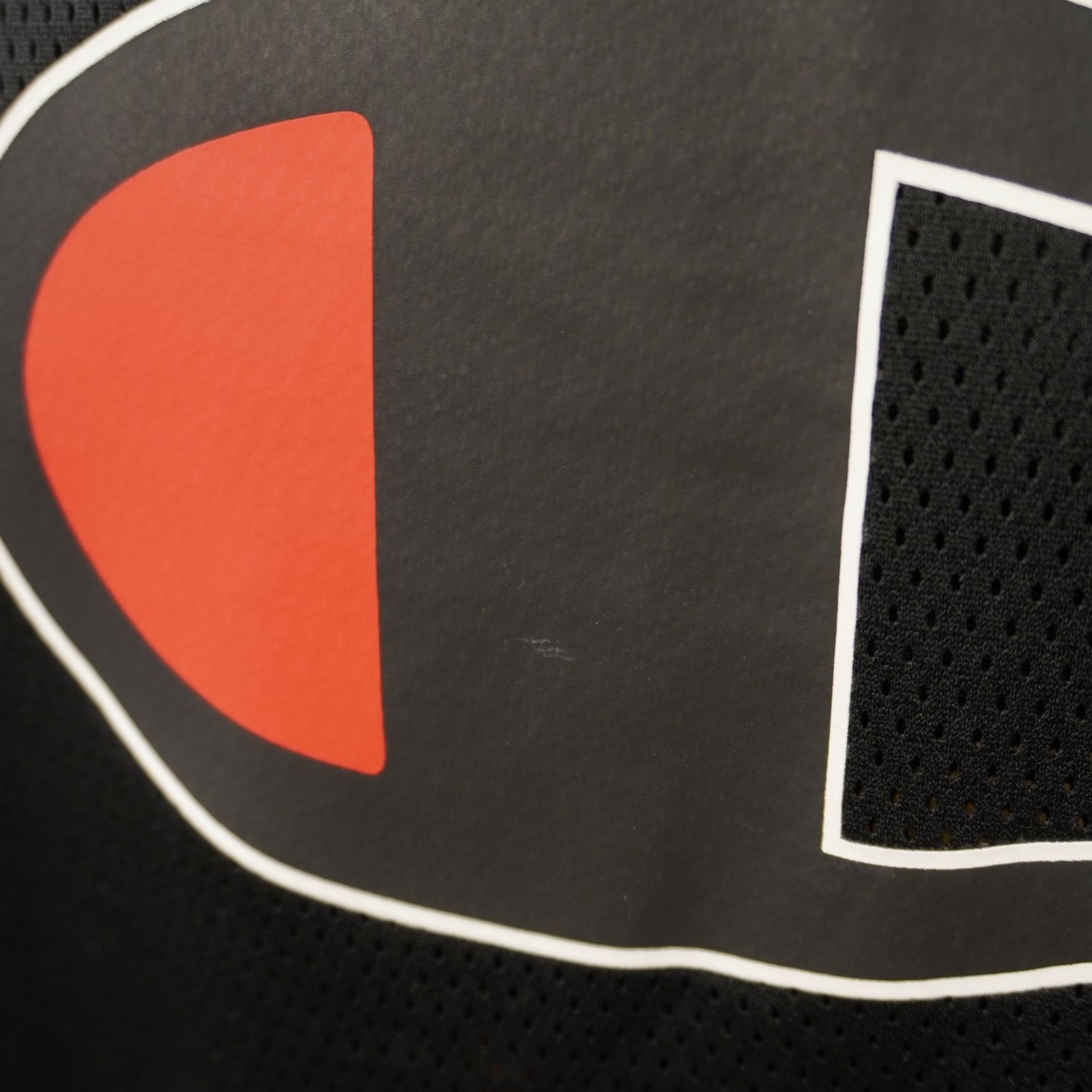 Primo piano ravvicinato dell'iconico maxi logo Champion rosso, bianco e nero ricamato al centro della maglia.