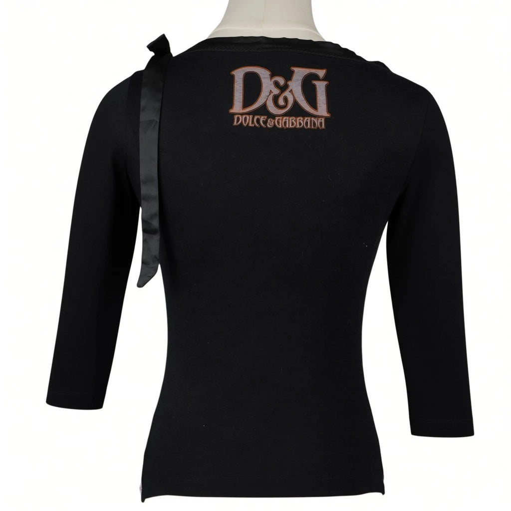 Vista posteriore completa della maglia nera D&G Dolce & Gabbana che mostra il maxi logo color bronzo e il fiocco sulla spalla.