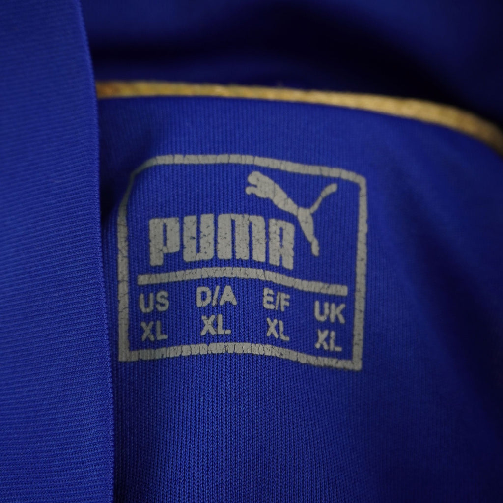 Dettaglio del logo dorato Puma e dell'etichetta interna termosaldata sotto il colletto della maglia.