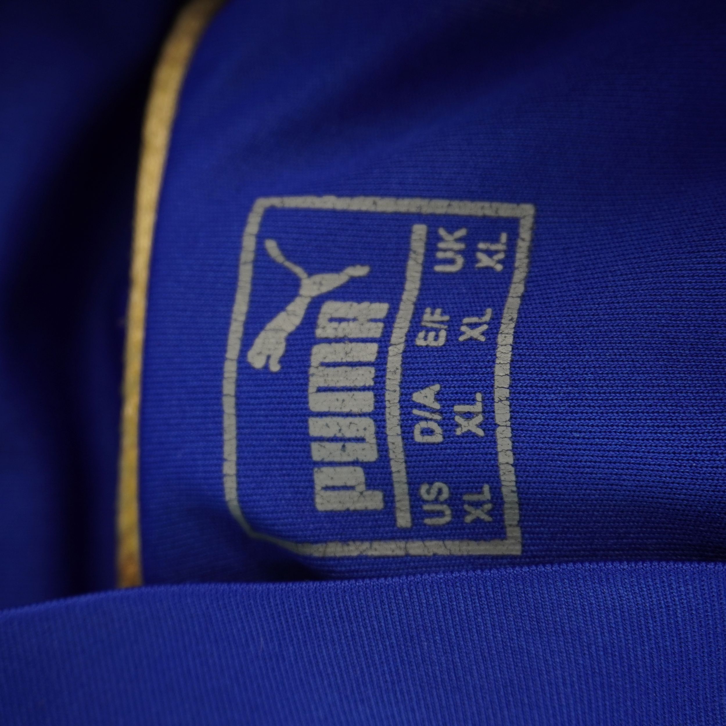 Dettaglio del logo dorato Puma e dell'etichetta interna termosaldata sotto il colletto della maglia.