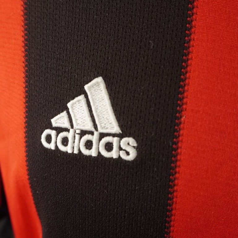 Primo piano del logo Adidas Performance ricamato in filo bianco sulla striscia verticale nera del petto della maglia del Milan.