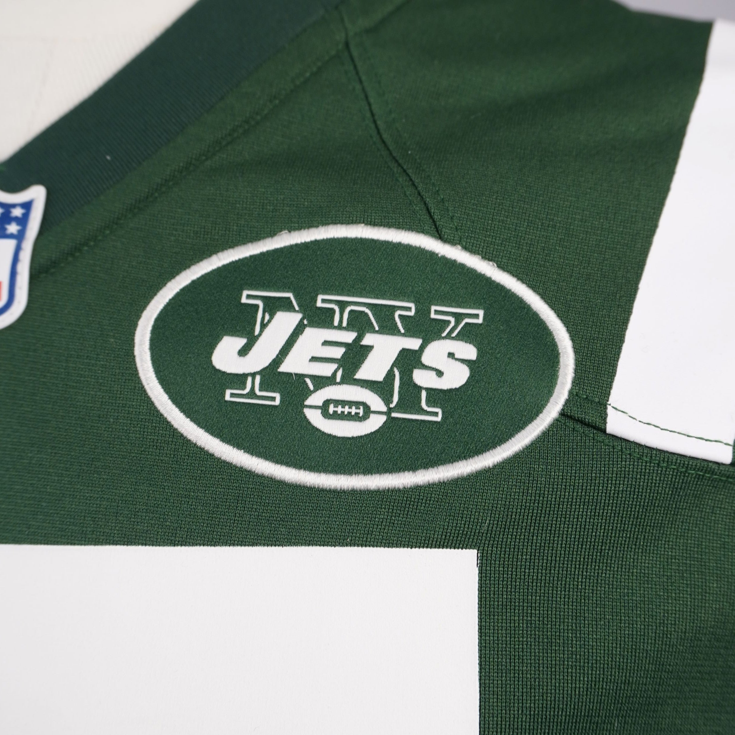 Primo piano macro della patch ovale ricamata con il logo dei New York Jets sul tessuto verde della maglia Nike.