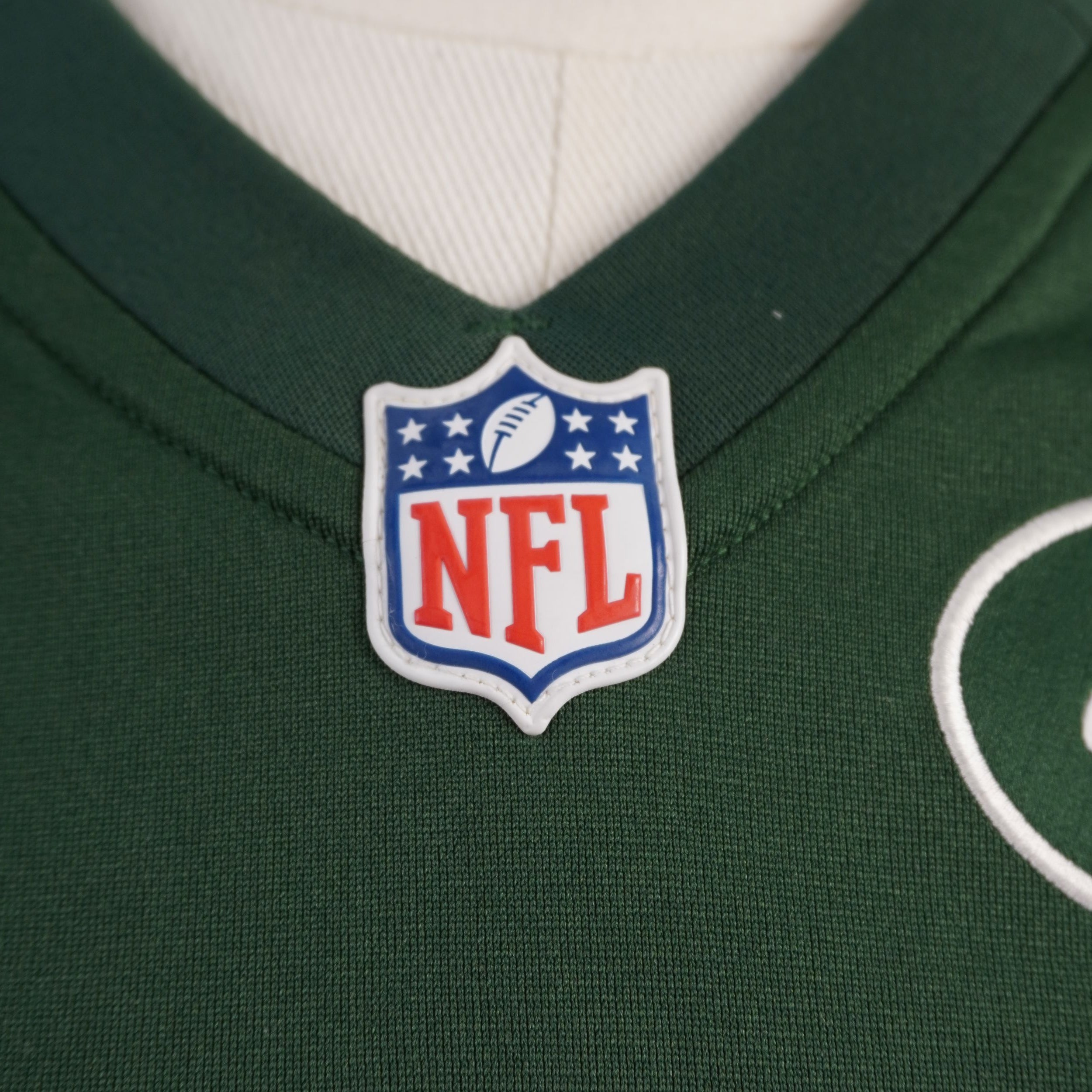 Primo piano dello scudetto ufficiale NFL gommato a rilievo applicato al centro del colletto a V della maglia da gioco.