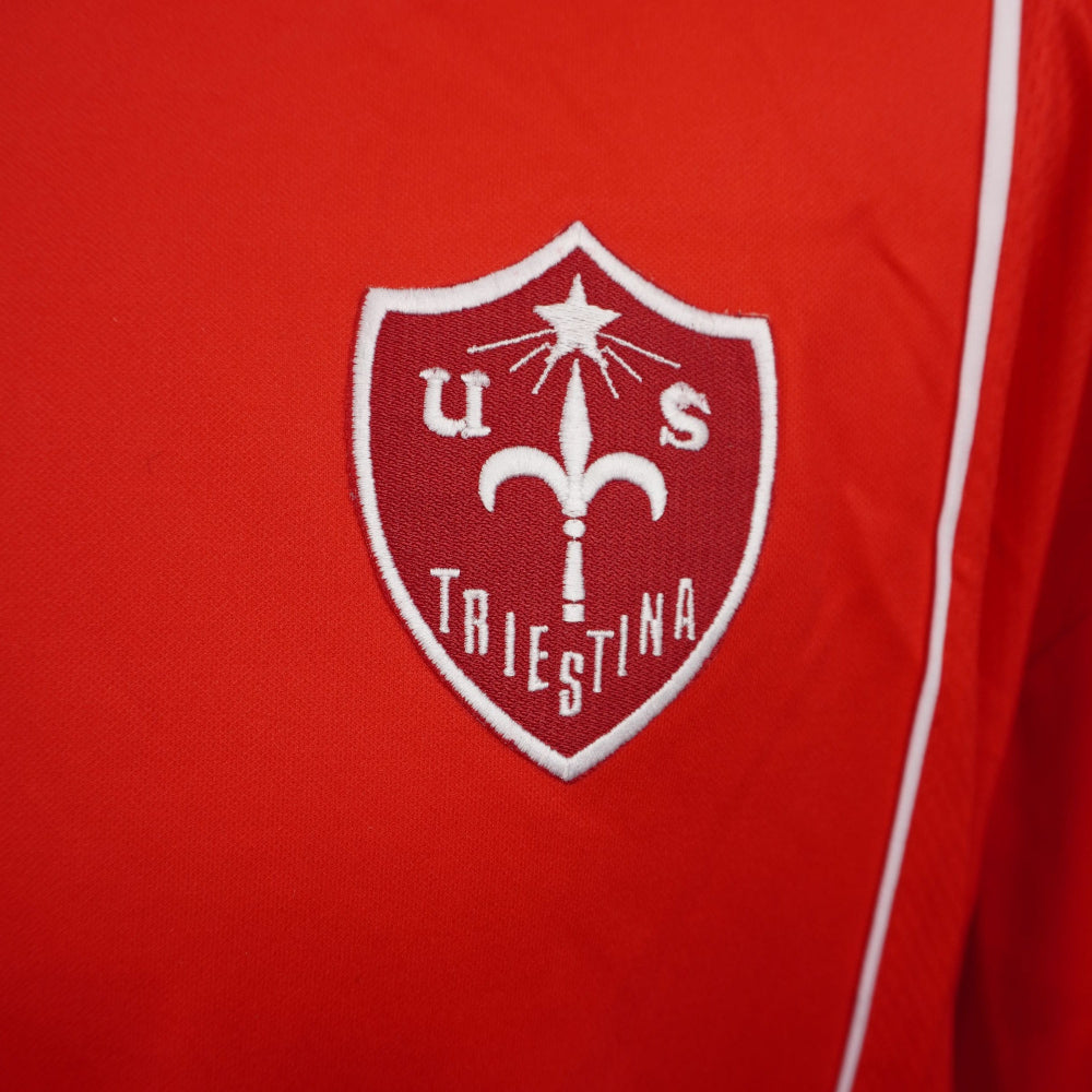 Primo piano dello stemma bianco e rosso della US Triestina Calcio ricamato a rilievo sul petto.