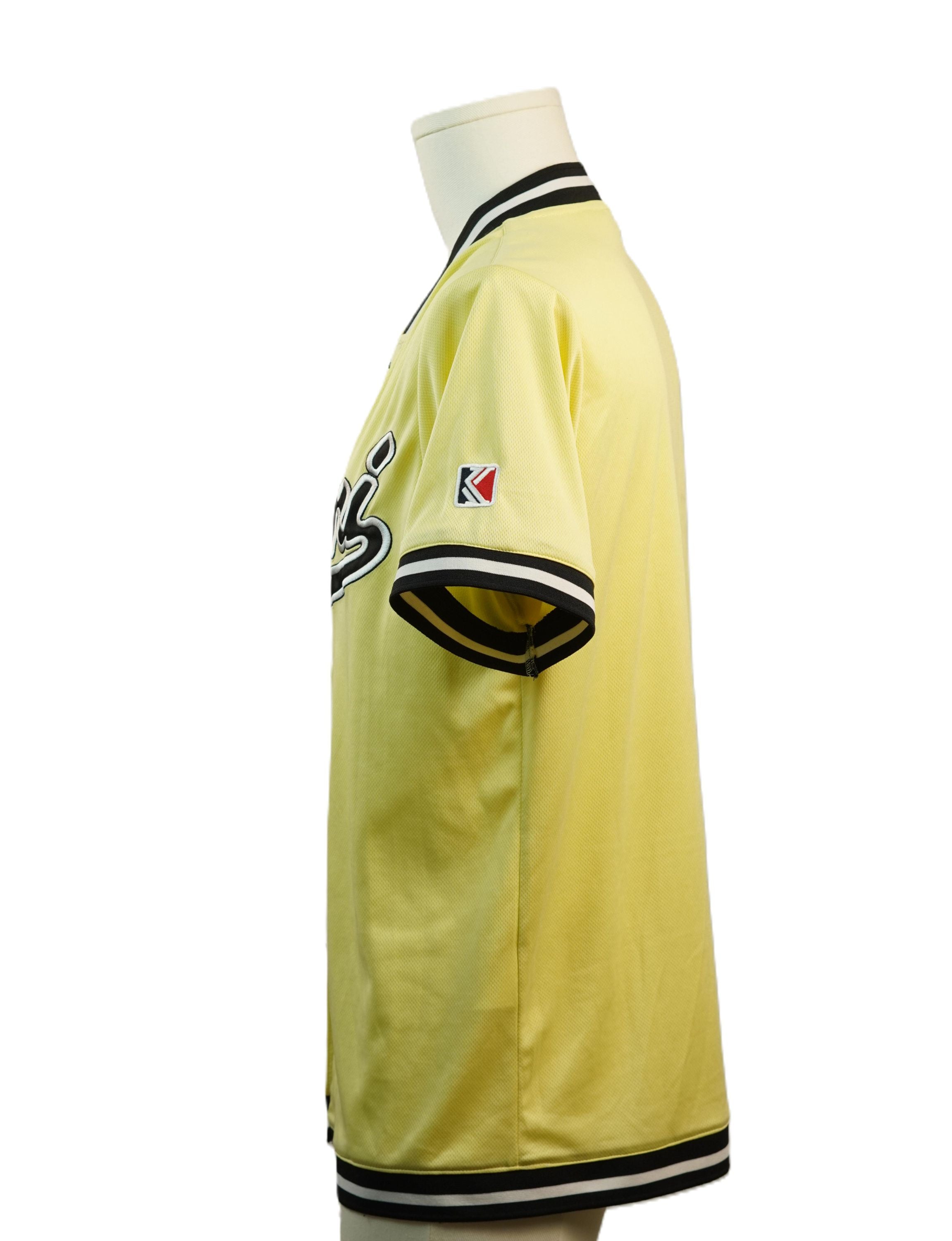 Vista laterale di profilo della maglia da baseball gialla sul manichino, che mostra la lunghezza della manica corta e la patch applicata sul braccio.
