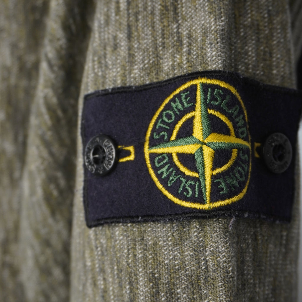 Primo piano del badge patch originale Stone Island ricamato sulla manica con bottoni logati neri.