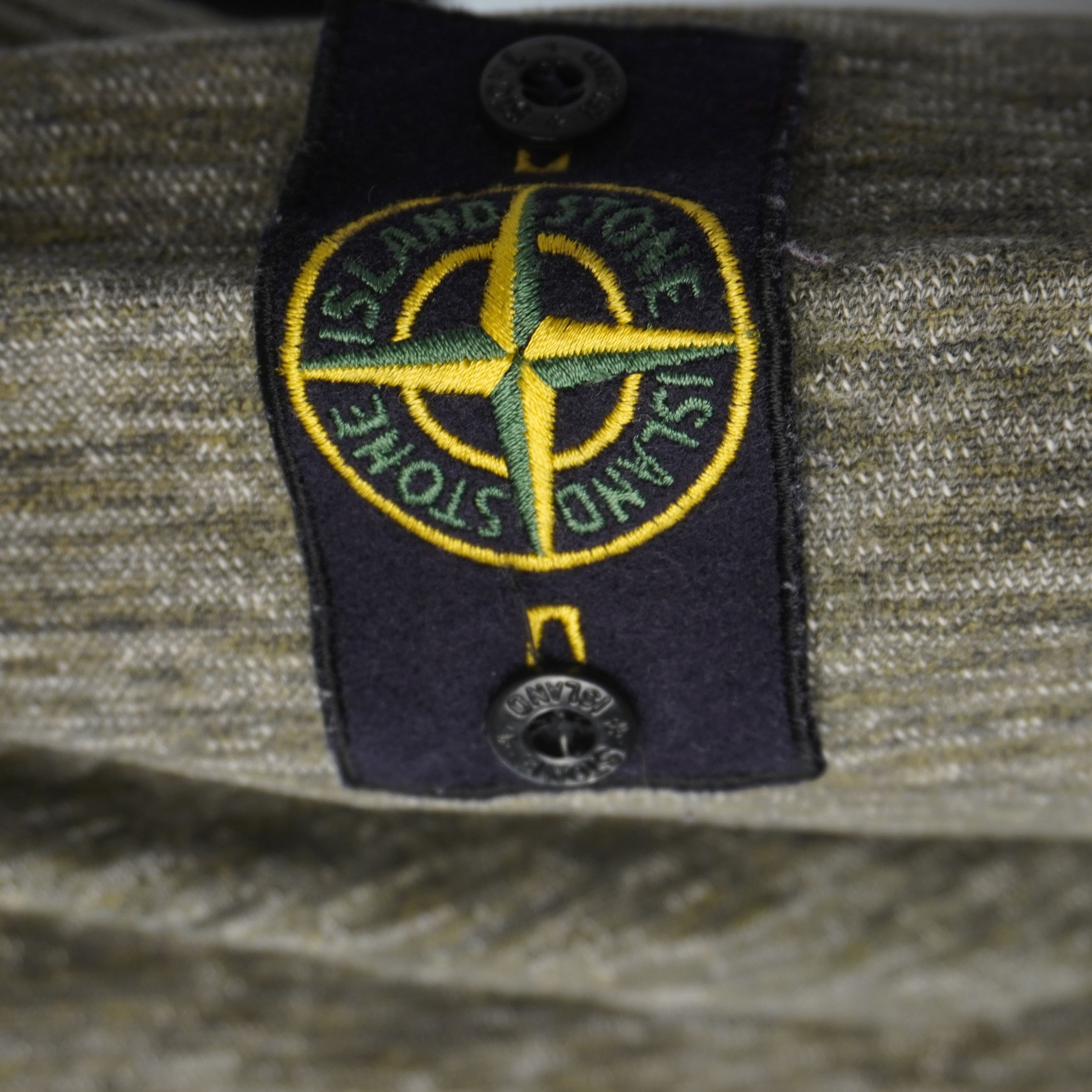 Primo piano del badge patch originale Stone Island ricamato sulla manica con bottoni logati neri.