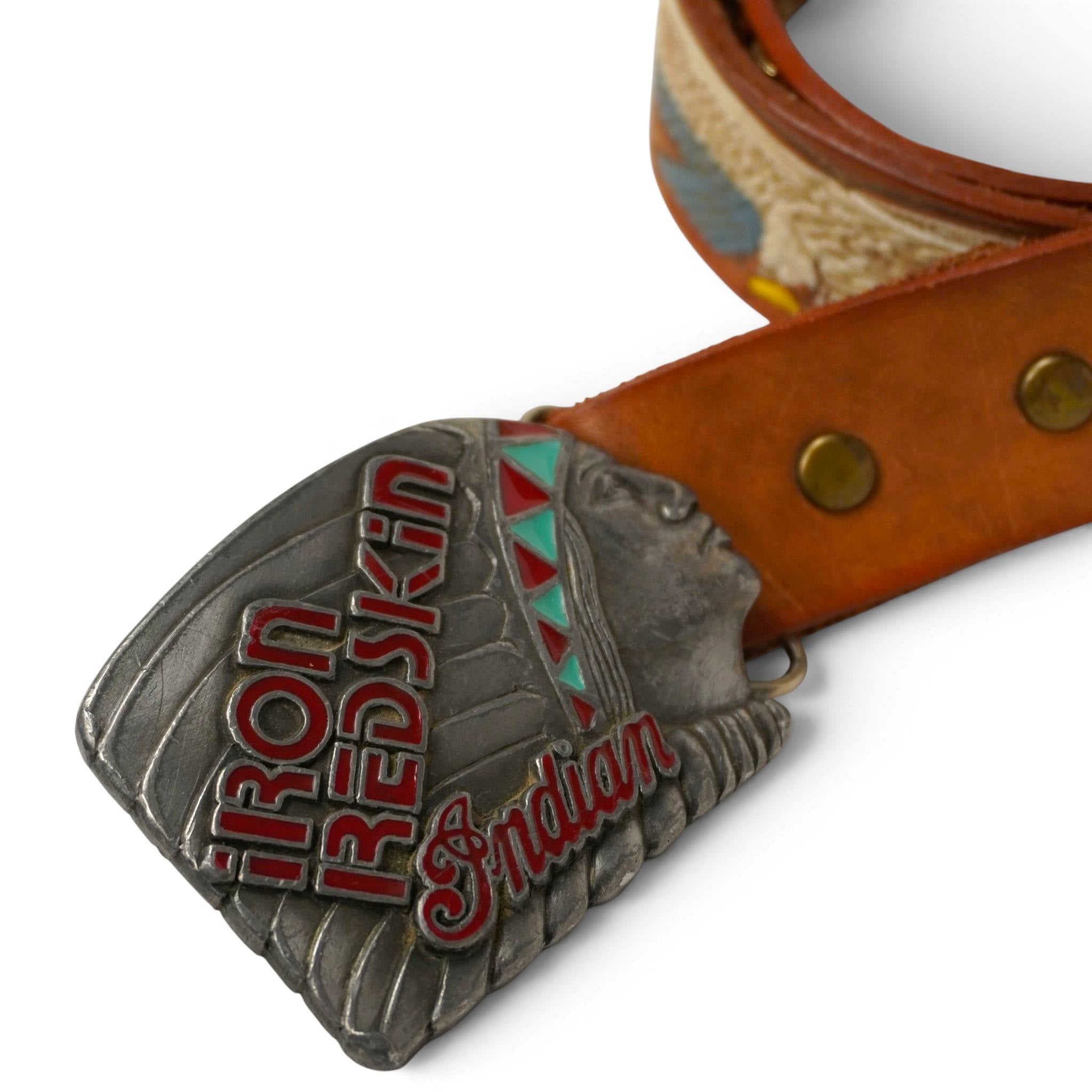 Primo piano della fibbia argentata Iron Redskin con profilo di capo indiano e dettagli geometrici tribali smaltati in rosso e azzurro.