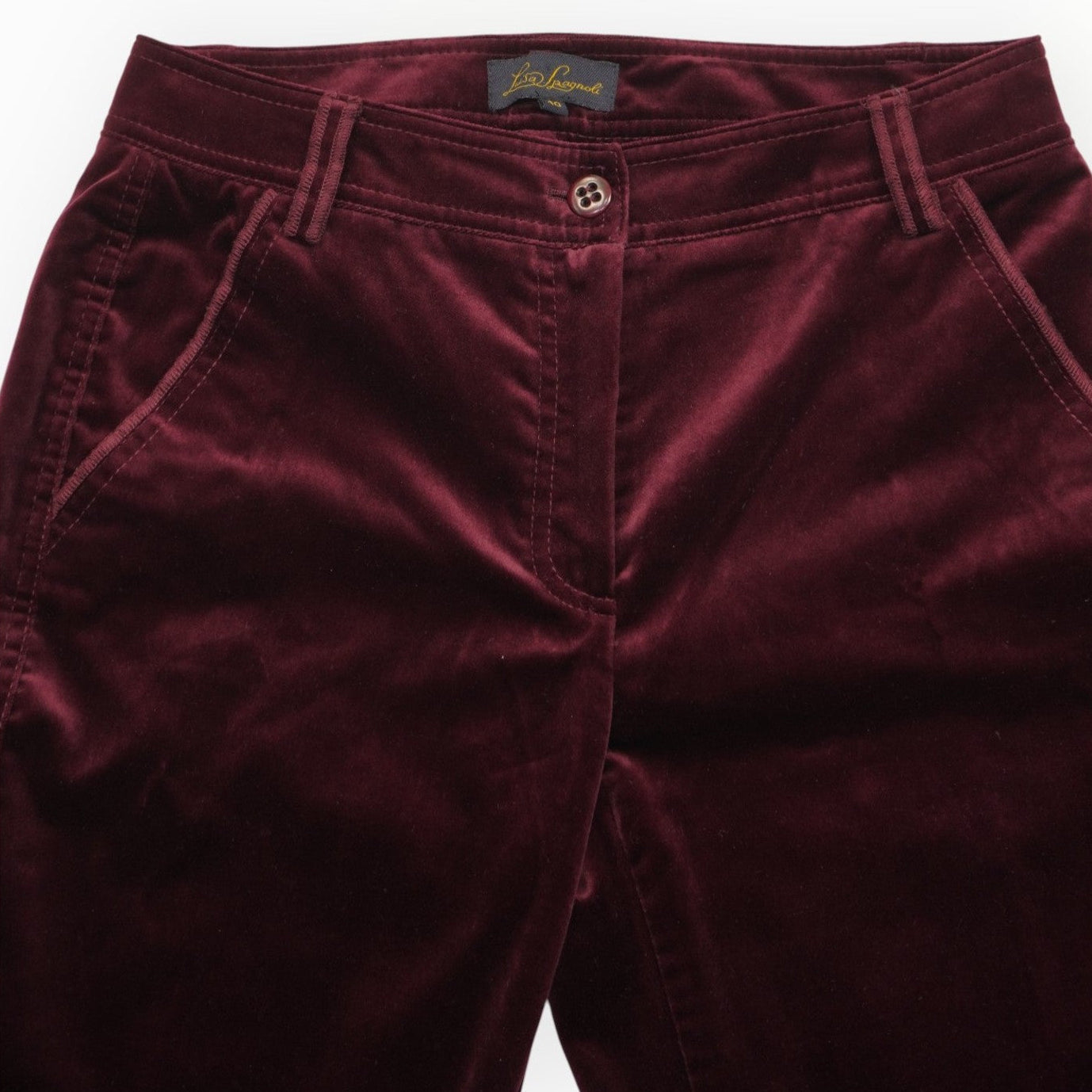 Inquadratura ravvicinata del girovita frontale dei pantaloni in velluto bordeaux con tasche laterali e bottone coordinato.