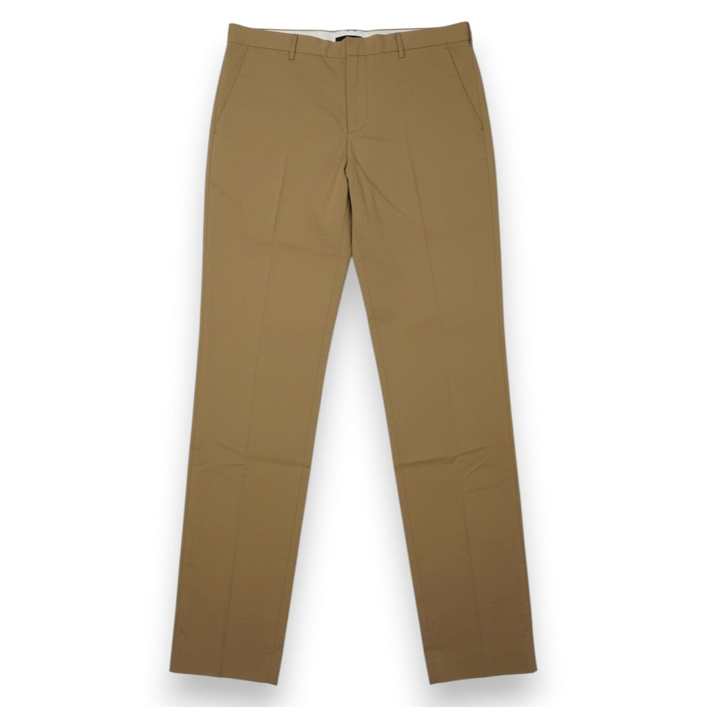 Vista frontale completa di pantaloni sartoriali Prada da uomo in cotone tecnico color beige cammello con piega centrale pressata.