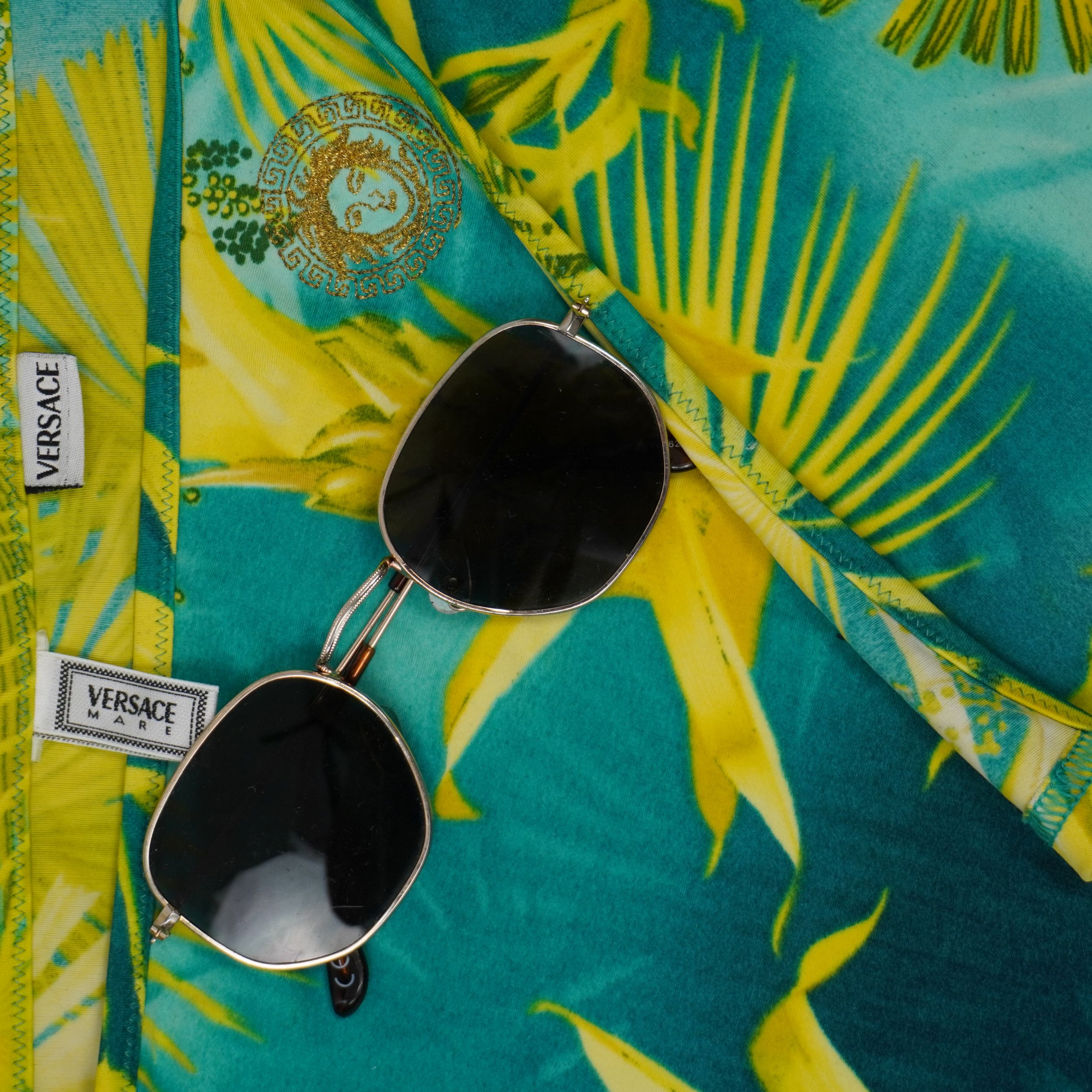 Inquadratura dall'alto del tessuto Jungle Print Versace con stemma della Medusa ricamato e occhiali da sole.
