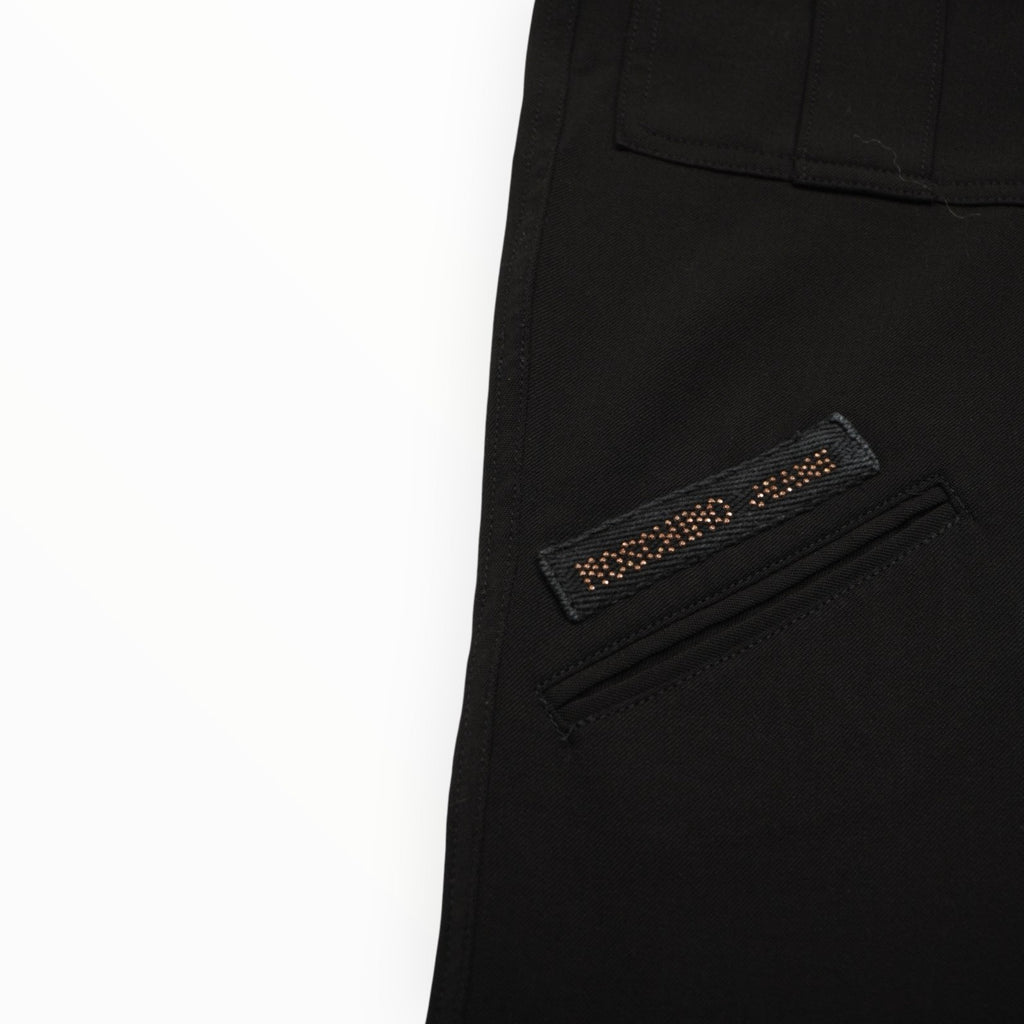 Close-up della patch logo in tessuto nero rettangolare Moschino Jeans applicata sulla coscia del pantalone.