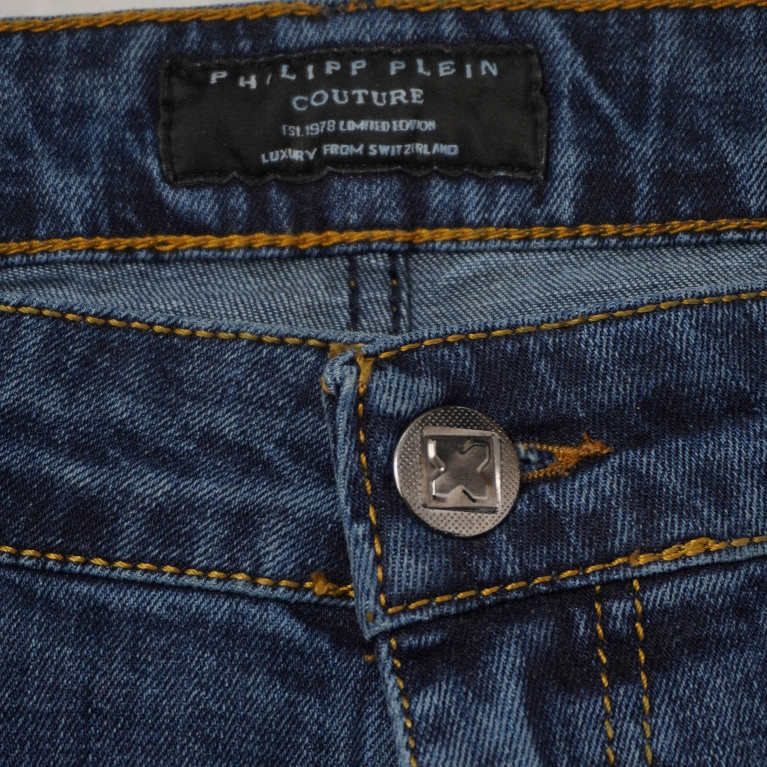 Primo piano del bottone metallico anteriore e dell'etichetta ricamata Philipp Plein Couture sulla cintura interna