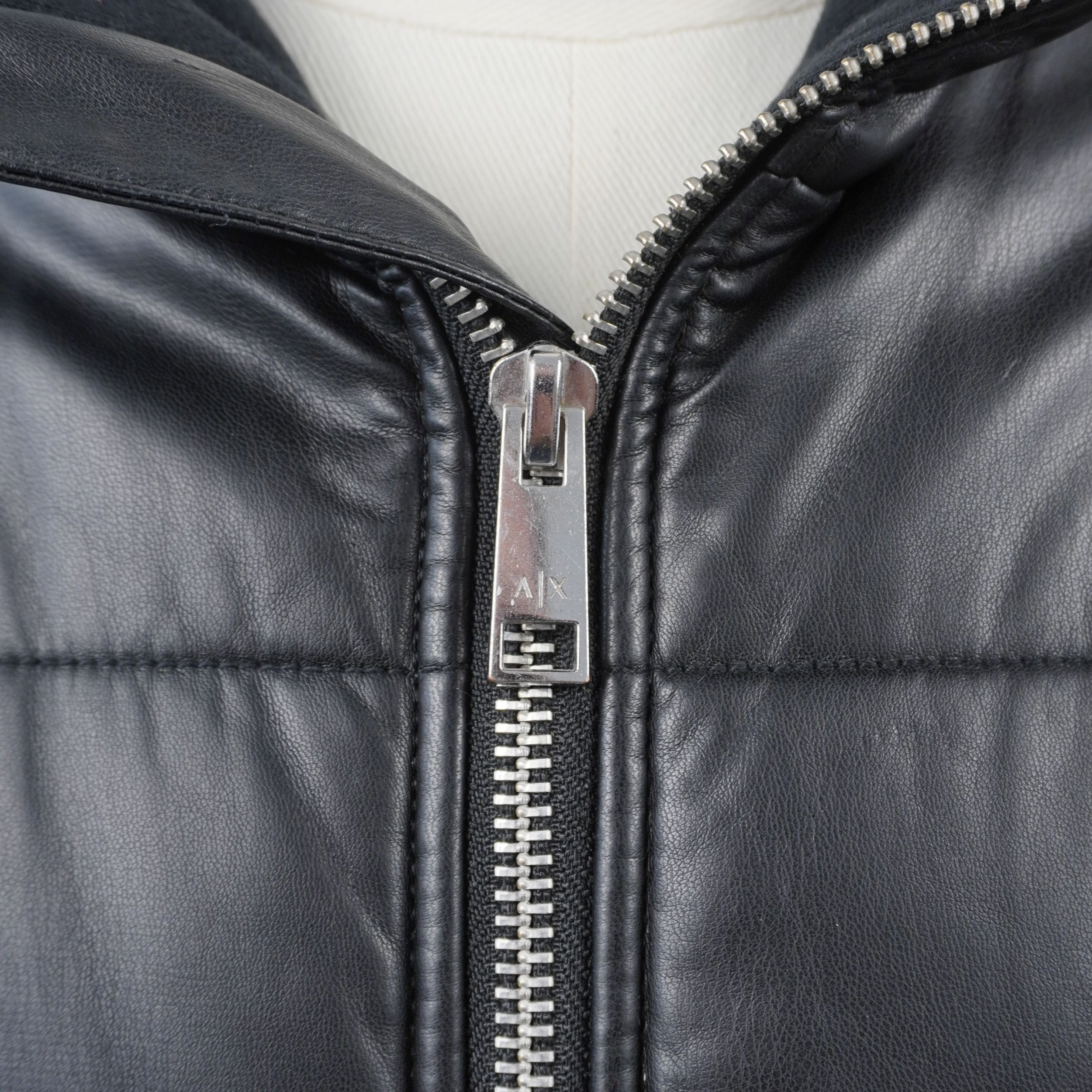 Primo piano del cursore della zip in metallo cromato con logo inciso AX del giubbotto Armani Exchange.