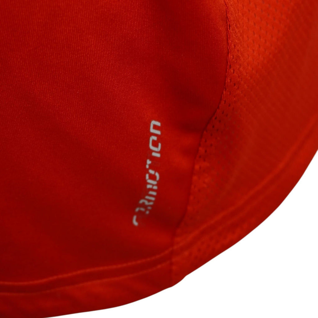 Dettaglio ravvicinato della stampa riflettente della tecnologia ClimaLite sul bordo inferiore della polo rossa Adidas.