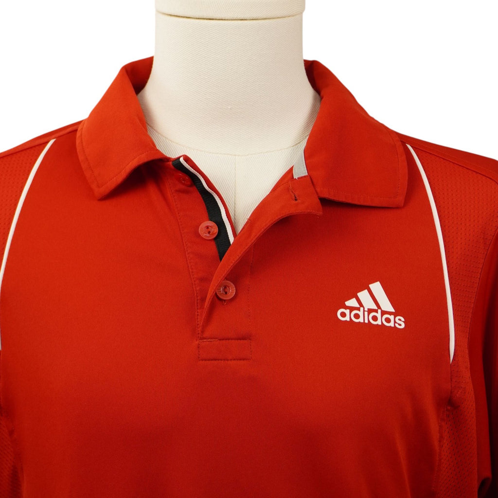 Primo piano del colletto a maglia e della chiusura a bottoni della polo rossa Adidas Barricade con ricamo del logo sul petto.