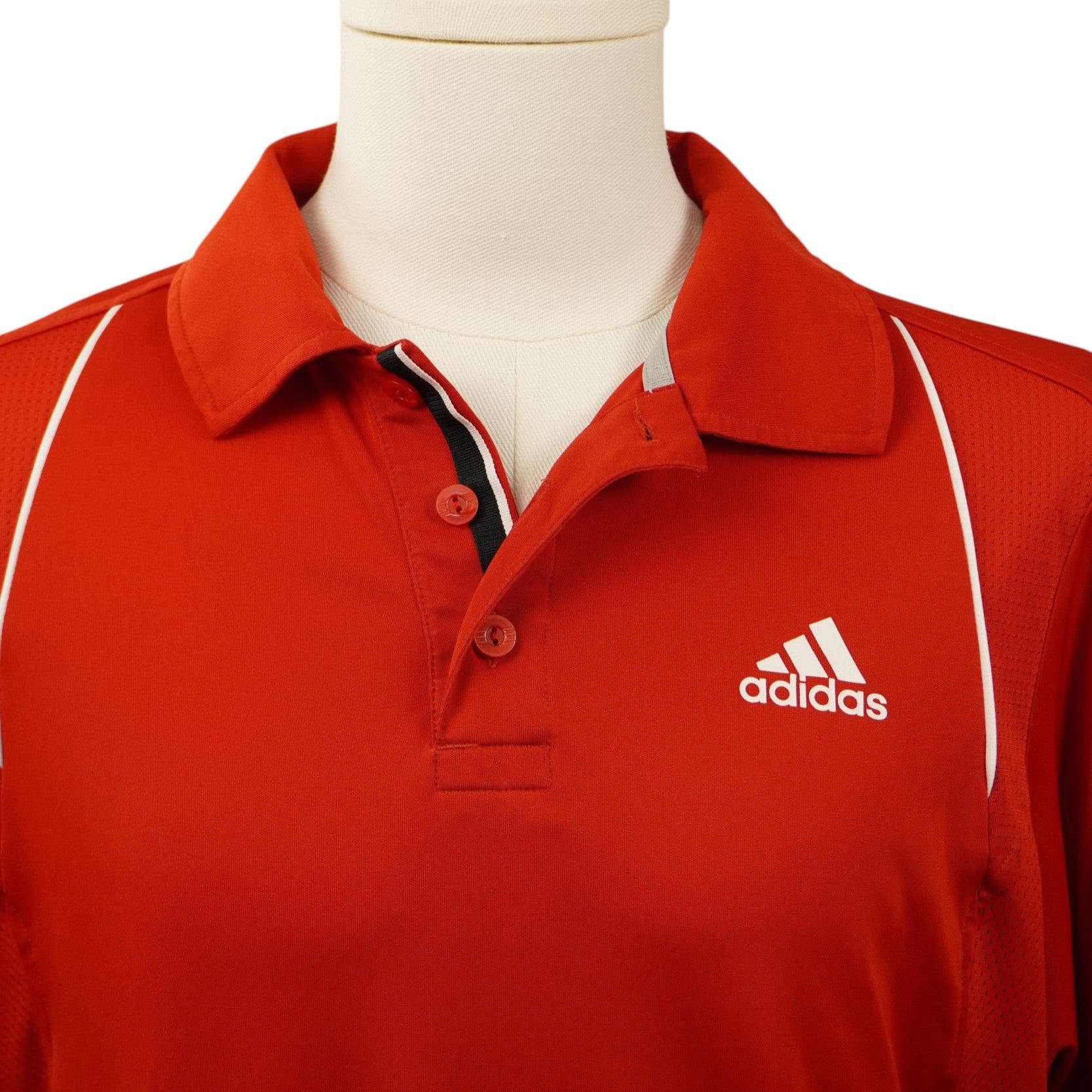 Primo piano del colletto a maglia e della chiusura a bottoni della polo rossa Adidas Barricade con ricamo del logo sul petto.