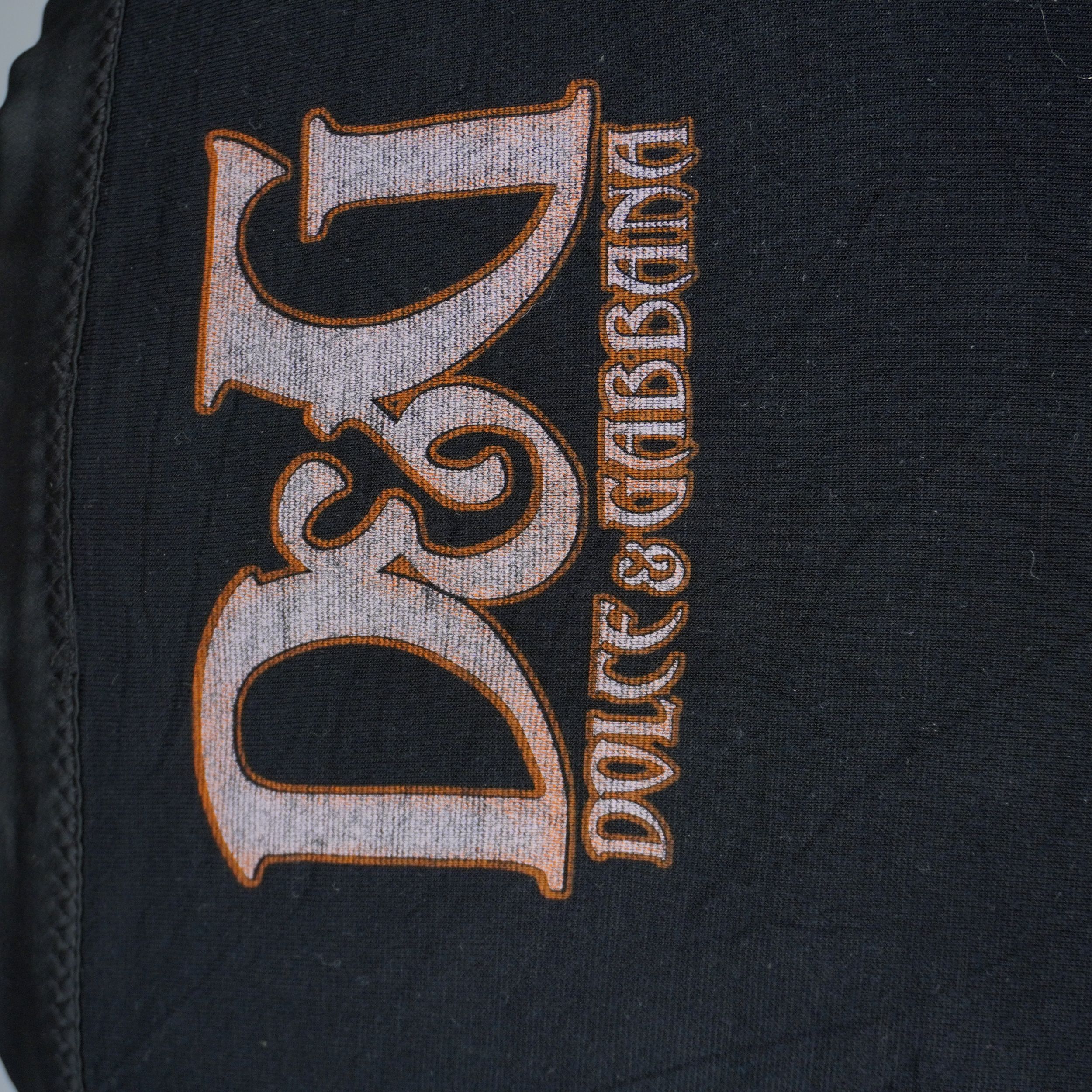 Macro sul maxi logo D&G Dolce & Gabbana stampato sul retro in tessuto nero con caratteri in stile gotico color bronzo.