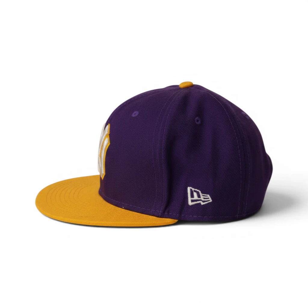 Profilo laterale sinistro del cappellino bicolore New Era con ricamo bianco della New Era Flag sulla corona viola e visiera gialla.