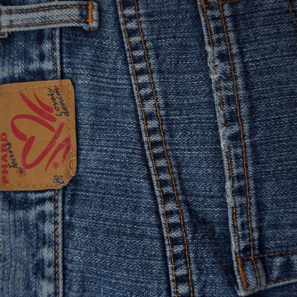 Dettaglio della salpa in pelle scamosciata marrone sul retro della vita con scritta Lovely Denim e cuore rosso.