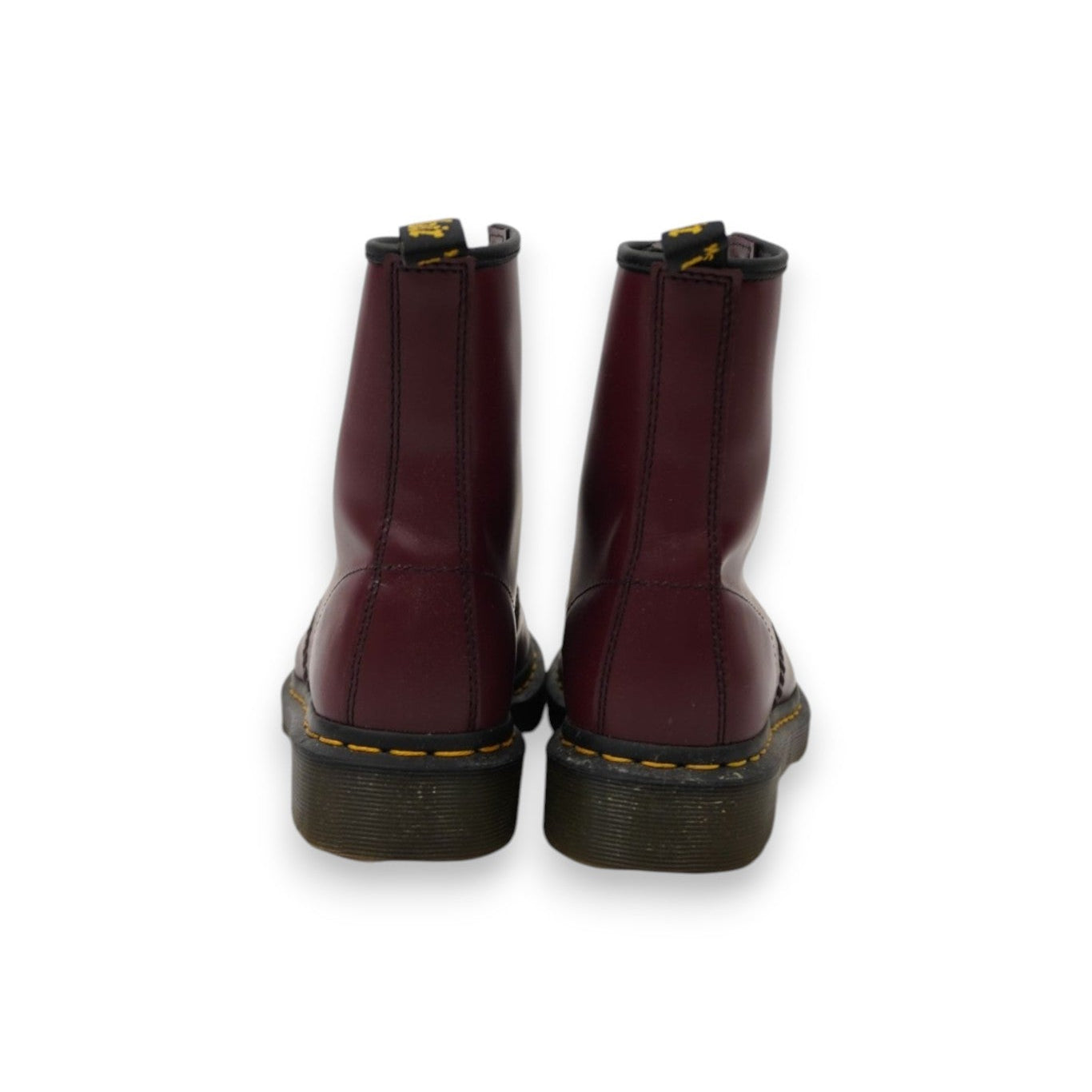 Vista posteriore del paio di anfibi Dr. Martens cherry red con focus sui talloni e sulla fettuccia logata AirWair nera e gialla.
