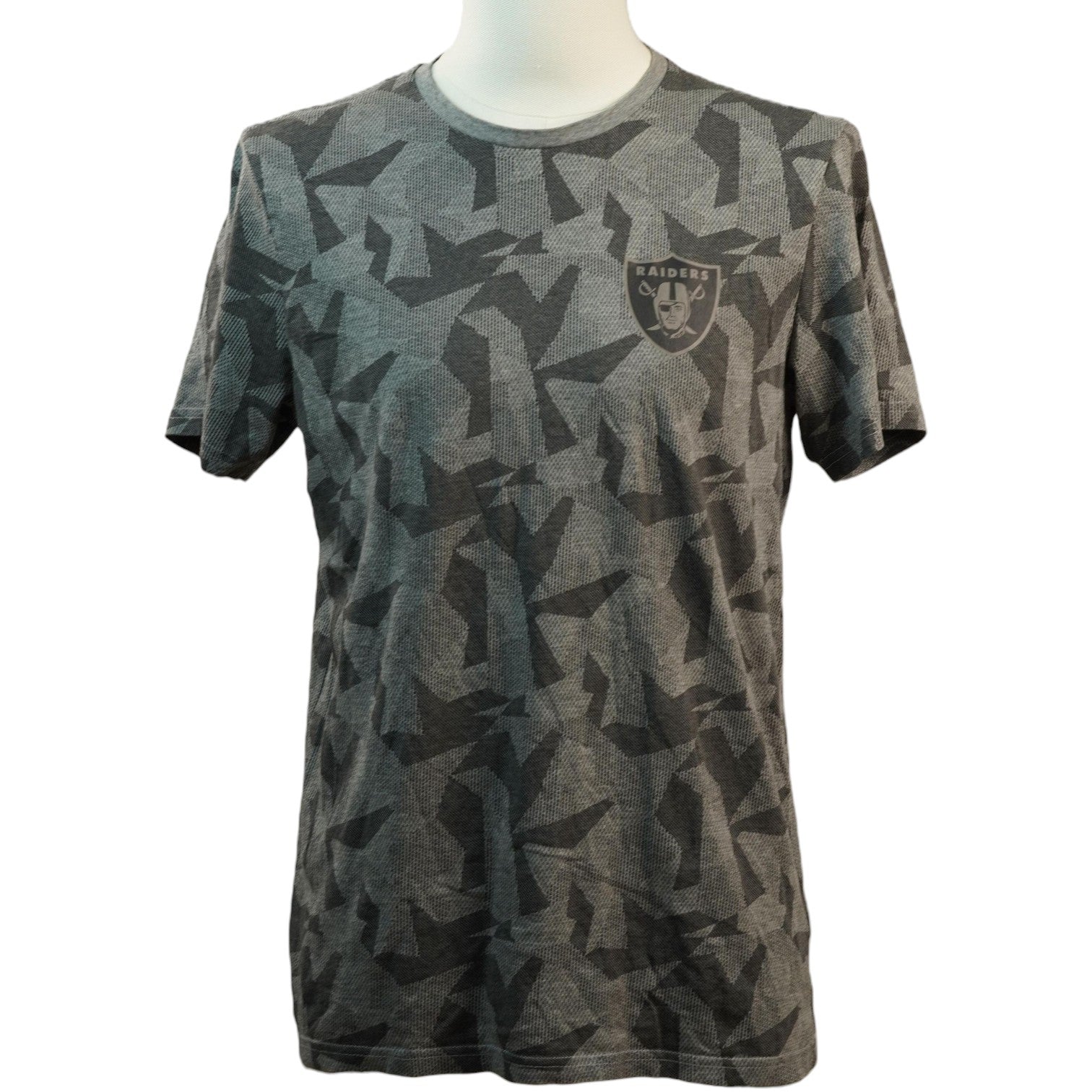 Vista frontale di una t-shirt grigia a maniche lunghe corte con stampa geometrica mimetica all-over, logo dei Las Vegas Raiders sul petto e manichino bianco.