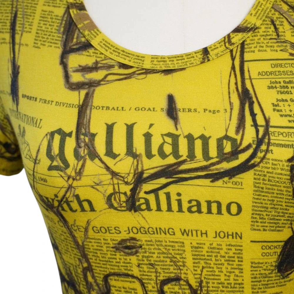 Primo piano del girocollo della t-shirt che mostra il logo Galliano stampato in carattere gotico sul tessuto giallo.
