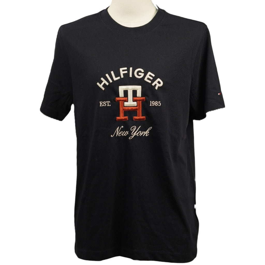 Vista frontale della t-shirt Tommy Hilfiger blu navy su manichino con grafica college ricamata arancione e bianca.