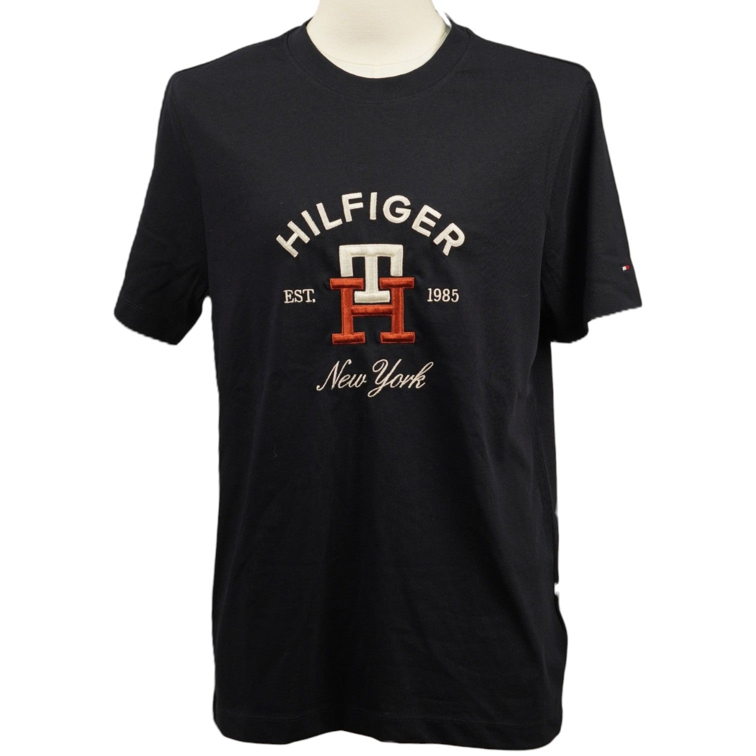 Vista frontale della t-shirt Tommy Hilfiger blu navy su manichino con grafica college ricamata arancione e bianca.