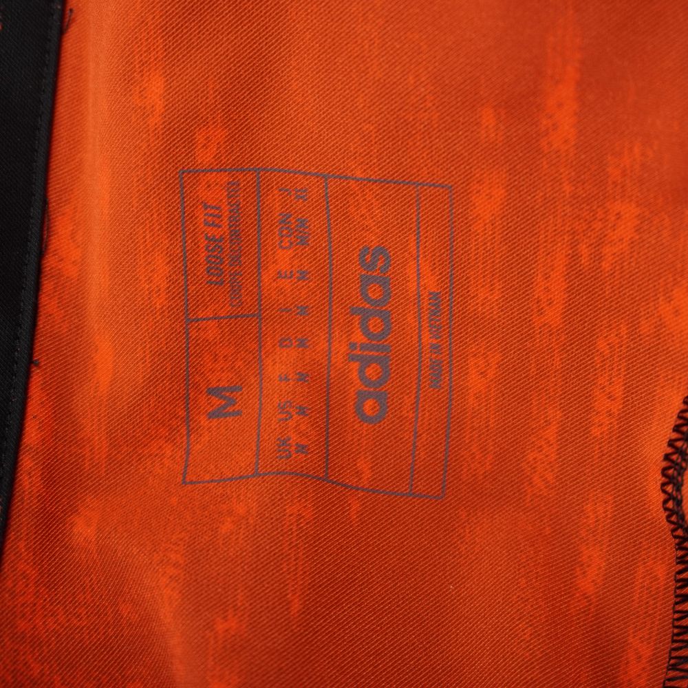 Inquadratura ravvicinata della stampa blu interna al collo che indica la taglia M, la vestibilità Loose Fit e il marchio Adidas.