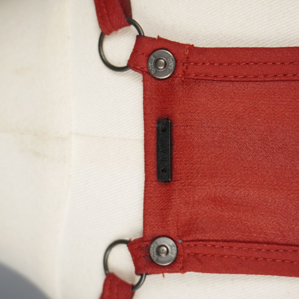  Ingrandimento del retro del top rosso con la placchetta in metallo nero RAW e i bottoni borchiati logati G-Star Raw alla base delle spalline.