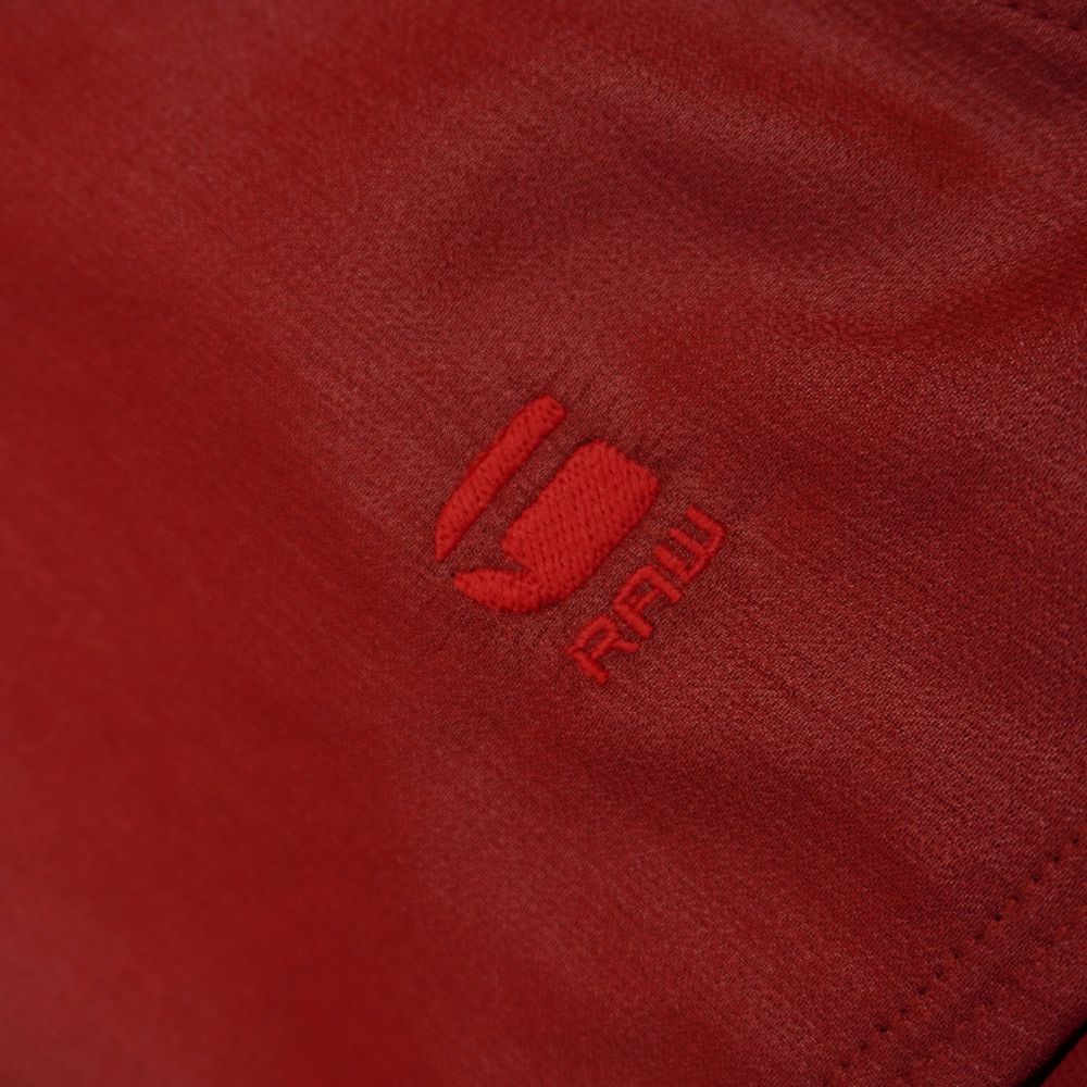 Primo piano del logo ufficiale con l'iconica lettera G e la scritta RAW ricamate con filo rosso in tinta sul tessuto.