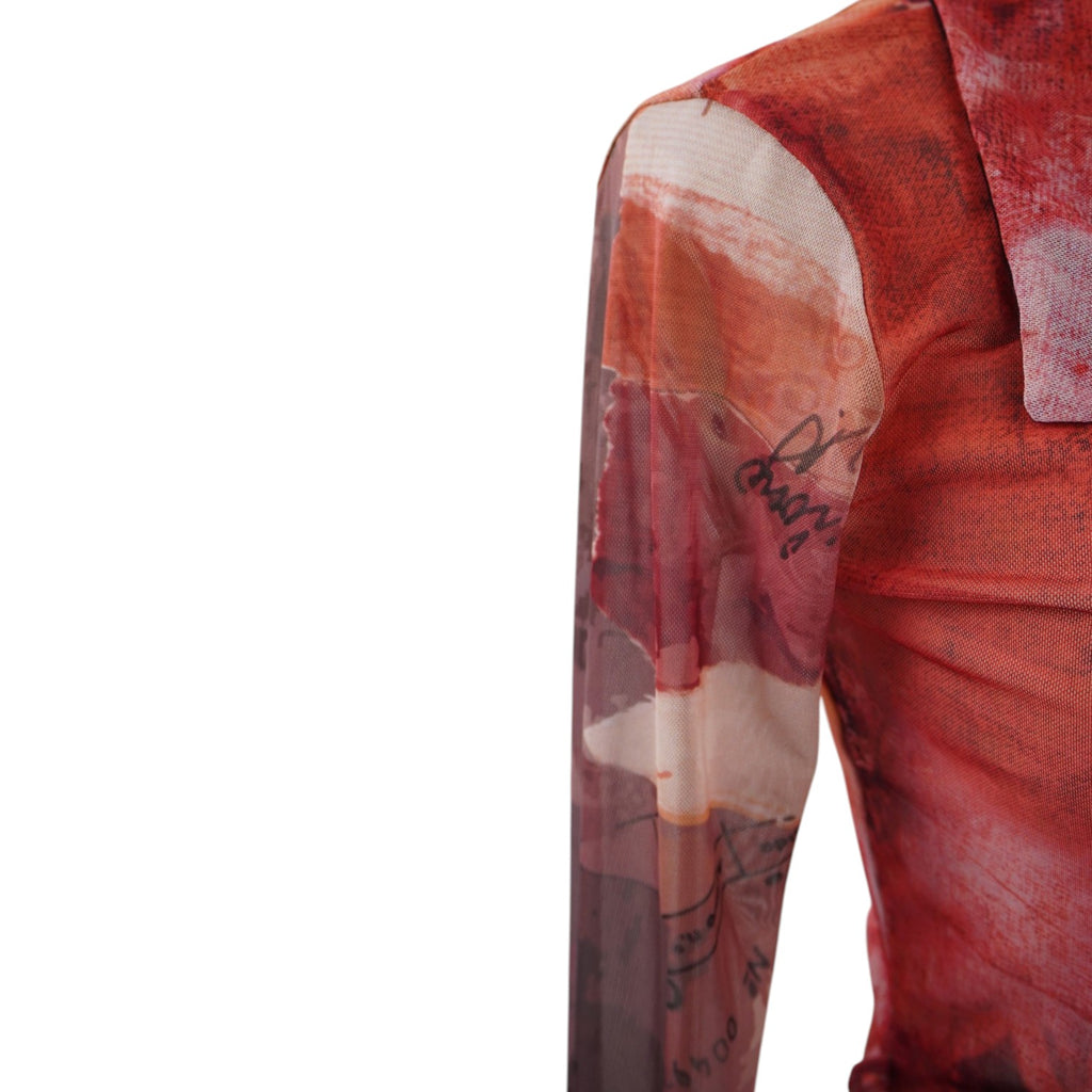 Particolare del tessuto in mesh semitrasparente e della manica lunga scivolata con stampa grafica nei toni del rosso e arancione
