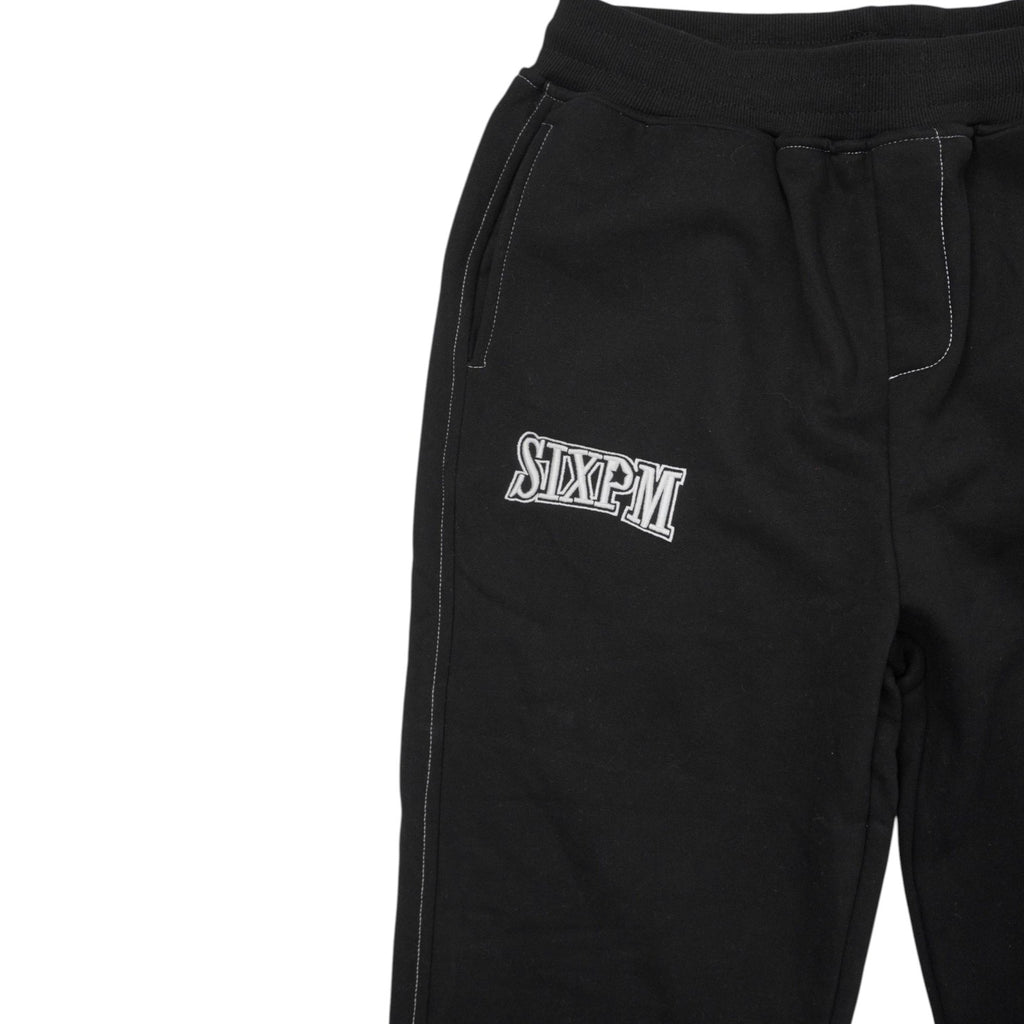 Particolare delle cuciture bianche a contrasto e della tasca ricamata sui pantaloni neri.