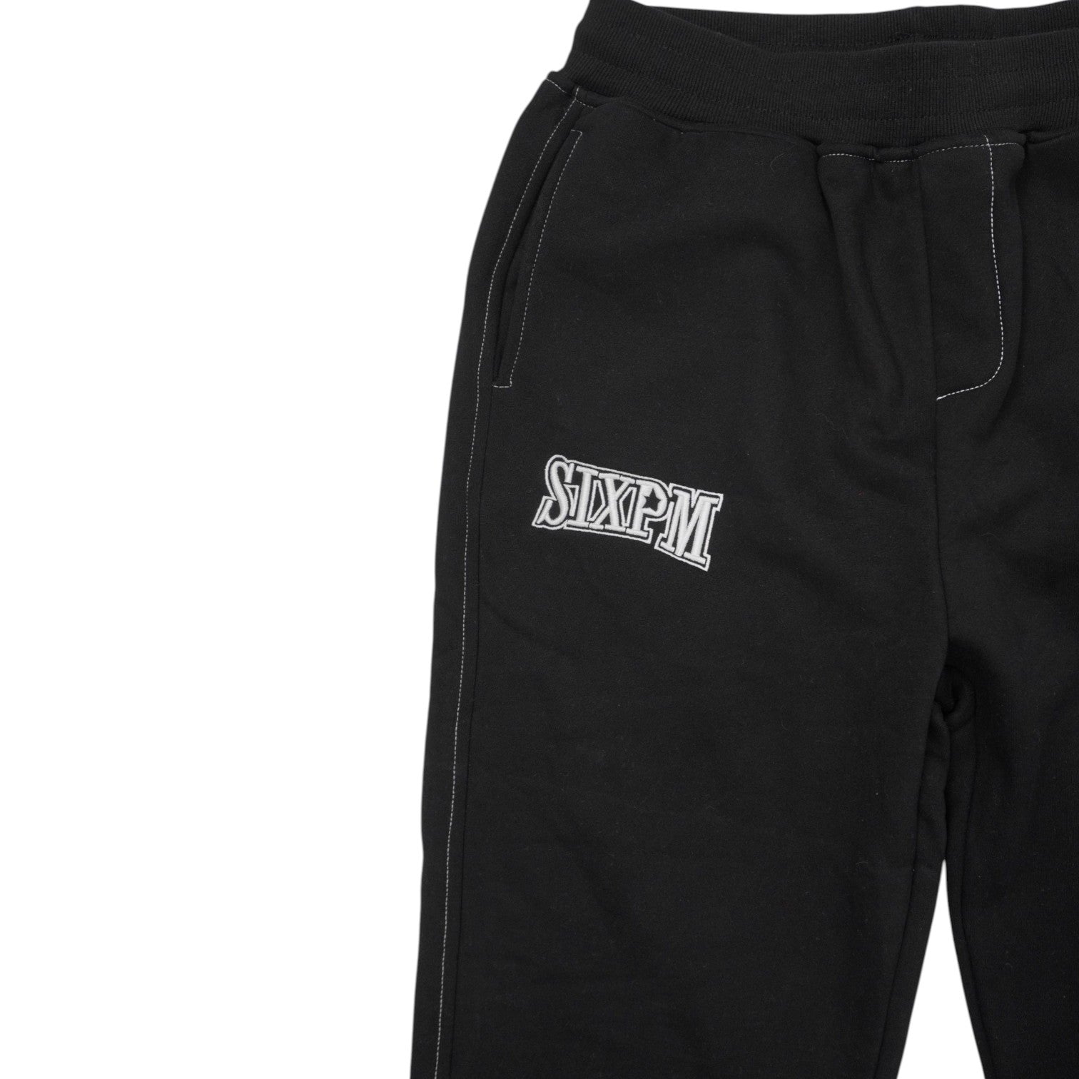 Particolare delle cuciture bianche a contrasto e della tasca ricamata sui pantaloni neri.