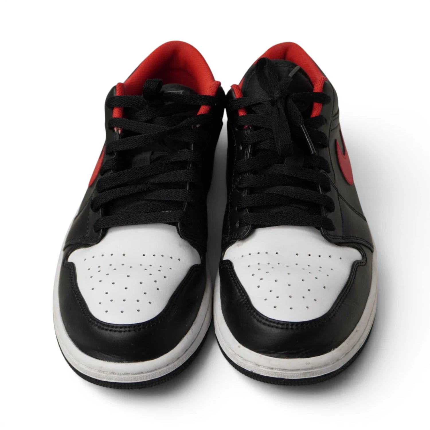 Inquadratura frontale simmetrica del paio di scarpe Air Jordan 1 Low con lacci neri e tomaia in pelle.