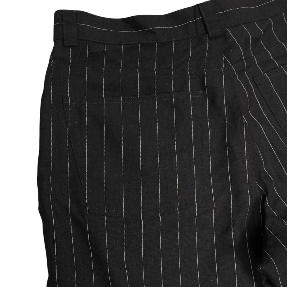 Inquadratura laterale ravvicinata dei pantaloni gessati neri Versus che mette in evidenza la trama e il pattern a righe verticali bianche.